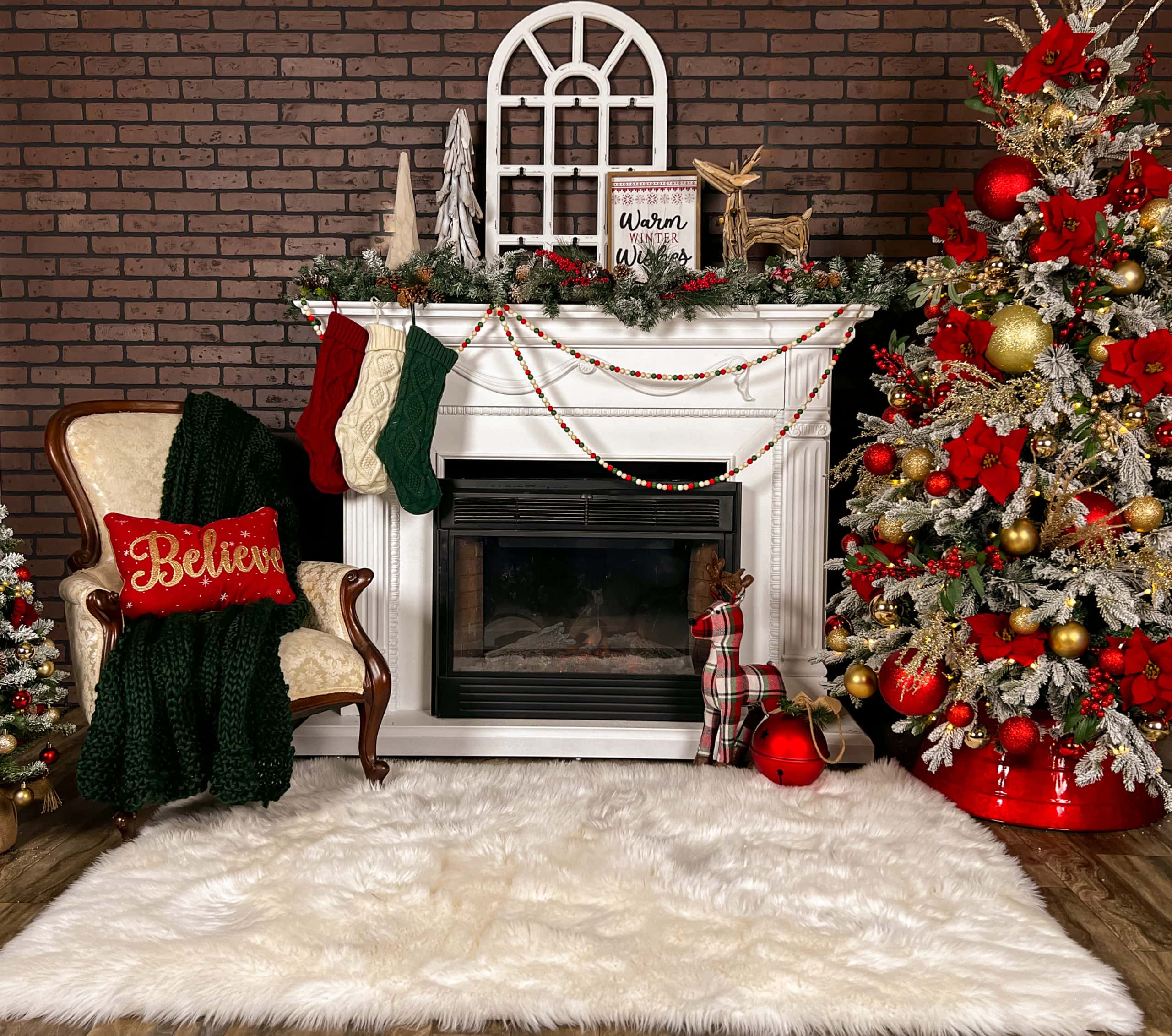 Photograph of a holiday themed photography background, centered by a white fireplace and with a Christmas tree to one side and an antique chair to the other side